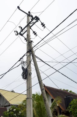 Bir sürü kablosu olan uzun bir elektrik direği. Kablolar karışık ve dağınık. Kutup bulutlu bir gökyüzü ile çevrilidir.