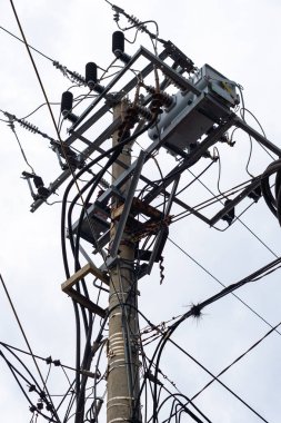 Bir sürü kablosu olan uzun bir elektrik direği. Kablolar karışık ve dağınık. Kutup bulutlu bir gökyüzü ile çevrilidir.