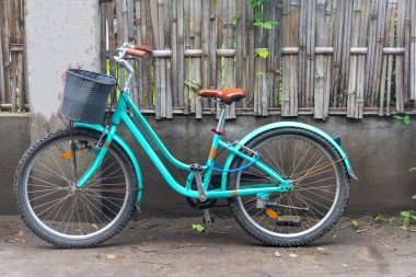 Önünde sepet olan mavi bir bisiklet. Sepet siyah ve bisiklet ahşap bir çite park edilmiş.