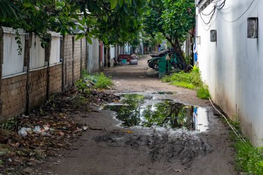 Su birikintileri ve arka planda duvar olan kirli bir yol. Manzara kasvetli ve ıssız.