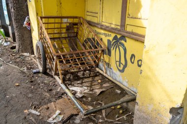 Gili, Lombok, Endonezya - 3 Ocak 2025: Paslı el arabası sarı bir binanın önünde oturuyor. Sahne, el arabasıyla kasvetli ve terk edilmiş.