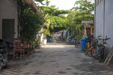 Gili, Lombok, Endonezya - 3 Ocak 2025: Birkaç sandalye ve birkaç bisikletle dar sokaklar. Sokaklar ağaçlarla kaplı ve birkaç tabela var.