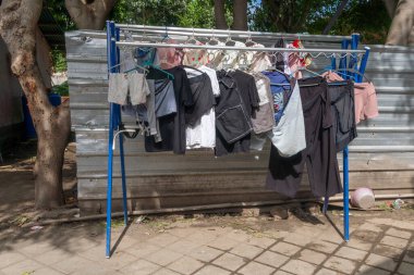 Çamaşır ipleri gömlekler, şortlar ve pantolonlar da dahil olmak üzere çeşitli giyim tarzlarıyla doludur. Giysiler bir binanın yakınındaki metal bir çamaşır ipine asılmış.