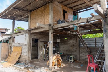 Önünde kırmızı bir sandalye olan harabe bir bina. Bina bakımsız görünüyor. Kırık camları ve çökmüş bir dış yüzeyi var.