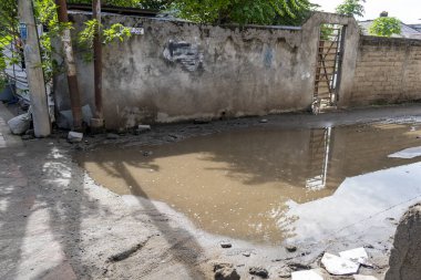 Su birikintileri ve arka planda duvar olan kirli bir yol. Manzara kasvetli ve ıssız.