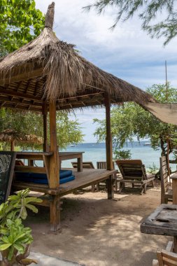 Üzerinde muşamba ve duvarında bir tabela olan sahil kulübesi. Kulübe ağaçlar ve sandalyelerle çevrili.