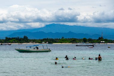 Gili, Lombok, Endonezya - 3 Ocak 2025: Bir grup insan bir teknenin yanında okyanusta yüzüyorlar. Su sakin ve berrak, gökyüzü bulutlu. Manzara huzurlu ve rahatlatıcı.