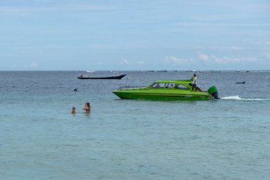 Gili, Lombok, Endonezya - 3 Ocak 2025: Bir grup insan bir teknenin yanında okyanusta yüzüyorlar. Su sakin ve berrak, gökyüzü bulutlu. Manzara huzurlu ve rahatlatıcı.