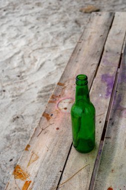 Gili, Lombok, Endonezya - 3 Ocak 2025: Yeşil bira şişesi ahşap bir bankta duruyor. Şişe boş ve tezgah grafiti ile kaplı.