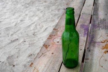 Gili, Lombok, Endonezya - 3 Ocak 2025: Yeşil bira şişesi ahşap bir bankta duruyor. Şişe boş ve tezgah grafiti ile kaplı.