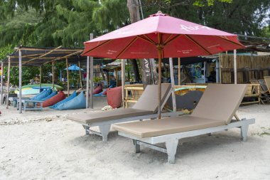 Gili, Lombok, Endonezya - 3 Ocak 2025: Kırmızı şemsiyeli ve iki bronz şezlonglu plaj. Sandalyeler boş.