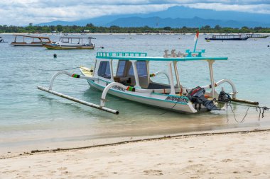 Gili, Endonezya - 3 Ocak 2025: Beyaz motorlu küçük tekne sahilde oturur. Tekne diğer teknelerle çevrilidir. Huzurlu ve huzurlu bir sahne.