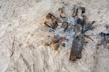 Kumlu bir sahilde odun ve kül yığını. Terk edilme ve ihmal kavramı. Tahta ve kül, sahilde çürümeye ve çürümeye terk edildi. Kamp ateşi için kullanıldıktan sonra tahta parçaları.