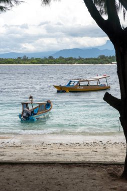Gili, Lombok, Endonezya - 3 Ocak 2025: Biri sarı olan ve AK yazan üç tekne sahile yanaştı. Diğer ikisi mavi ve beyaz. Su sakin ve gökyüzü bulutlu.