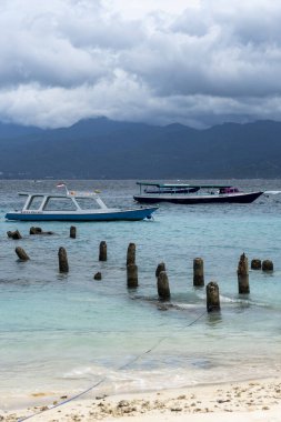 Gili, Lombok, Endonezya - 3 Ocak 2025: Tekne bir rıhtımın yanında suda oturuyor. Gökyüzü bulutlu ve su mavi.