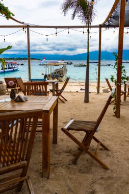 Gili, Lombok, Endonezya - 3 Ocak 2025: Tahta masa ve sandalyeli plaj. Sandalyeler boş. Masa bir masa örtüsüyle kaplı.