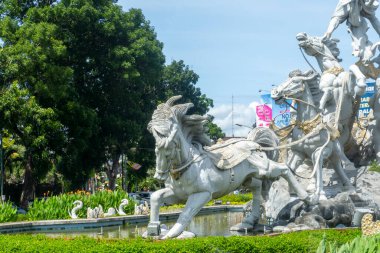 Bali, Endonezya - 19 Aralık 2024: bir at heykeli ve sırtında iki adam. Heykel yemyeşil bir park ile çevrili.