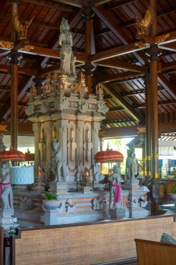 Bali, Endonezya - 19 Aralık 2024: Ortasında bir heykel ve köşesinde bir Noel ağacı olan büyük bir oda. Oda birçok lambayla süslenmiş ve sıcak, davetkar bir atmosferi var.