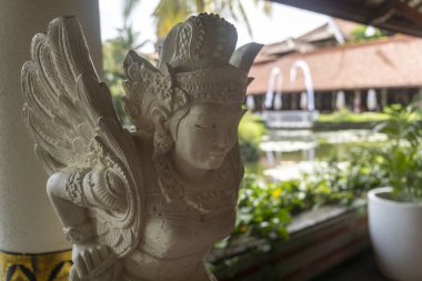 Bali, Endonezya - 19 Aralık 2024: Bir kadının heykeli bir otelin içinde kaidedir. Heykel bitkiler ve bir çeşmeyle çevrilidir. Heykelle manzara huzurlu ve huzurlu.