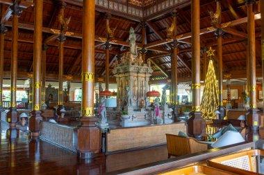 Bali, Endonezya - 19 Aralık 2024: Ortasında bir heykel ve köşesinde bir Noel ağacı olan büyük bir oda. Oda birçok lambayla süslenmiş ve sıcak, davetkar bir atmosferi var.