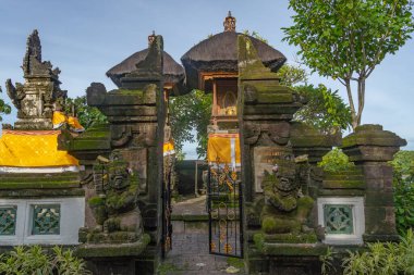 Bali, Endonezya - 19 Aralık 2024: Tapınağın girişi yosunlarla kaplı ve her iki tarafında iki erkek heykeli var. Kapı açık ve gökyüzü açık.