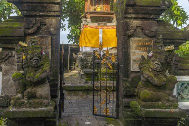 Bali, Endonezya - 19 Aralık 2024: Tapınağın girişi yosunlarla kaplı ve her iki tarafında iki erkek heykeli var. Kapı açık ve gökyüzü açık.