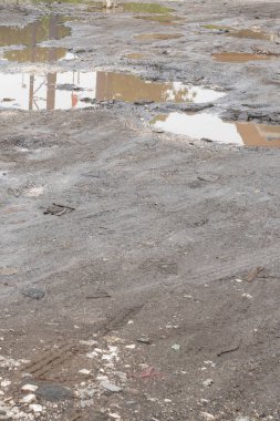 Su birikintileri ve molozlarla dolu çamurlu bir yol. Manzara kasvetli ve ıssız.