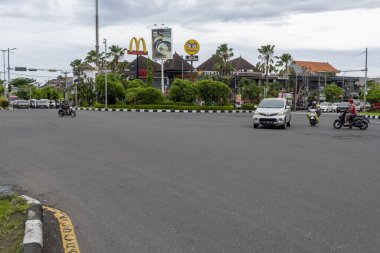 Bali, Endonezya - 25 Aralık 2024: Arka planda McDonald 's tabelası olan işlek cadde. Sokakta arabalar ve motosikletler sürüyor.