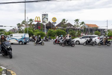 Bali, Endonezya - 25 Aralık 2024: Arka planda McDonald 's tabelası olan işlek cadde. Sokakta arabalar ve motosikletler sürüyor.