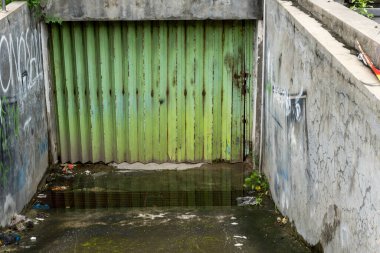Bali, Endonezya - 25 Aralık 2024: Kirli, terk edilmiş bir sokak ve yeşil metal bir kapı. Kapı açık ve yerde bir su birikintisi var.