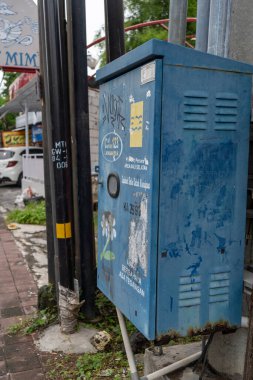 Bali, Endonezya - 25 Aralık 2024: Üzerinde grafiti olan mavi elektrik kutusu kaldırımda duruyor. Kutu bir bina ve bir arabanın yanında.