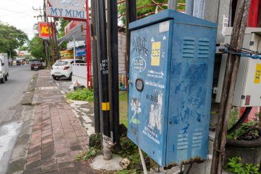 Bali, Endonezya - 25 Aralık 2024: Üzerinde grafiti olan mavi elektrik kutusu kaldırımda duruyor. Kutu bir bina ve bir arabanın yanında.