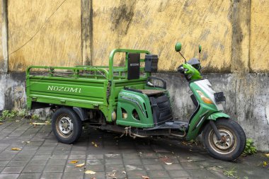 Bali, Endonezya - 25 Aralık 2024: Üzerinde NOZOMI yazan yeşil scooter yolun kenarına park edilmiştir. Scooter bir duvarın yanına park edilmiş ve üç tekerlekli küçük bir araç.