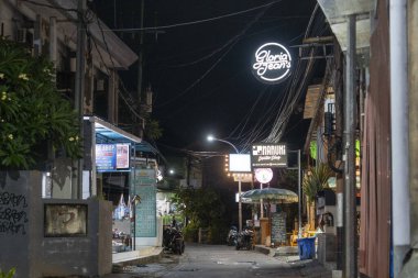 Bali, Endonezya - 25 Aralık 2024: Kuta, Bali 'de üzerinde Gloria Jeans yazan karanlık sokak. Sokak boş ve sessiz, sadece birkaç motosiklet ve birkaç şemsiyeyle.