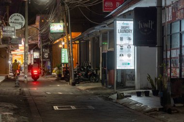 Bali, Endonezya - 25 Aralık 2024: Kuta, Bali 'de üzerinde bir çamaşırhane tabelası asılı olan karanlık sokak. Sokak boş ve sessiz, sadece birkaç motosiklet park etmiş..