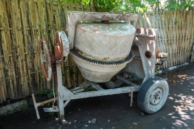 Paslı tekerleği olan çimento karıştırıcısı bahçede duruyor. Tekerlek kayıp ve makine bakımsız.