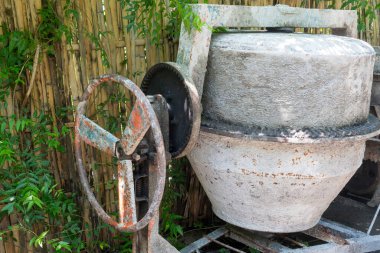 Paslı tekerleği olan çimento karıştırıcısı bahçede duruyor. Tekerlek kayıp ve makine bakımsız.