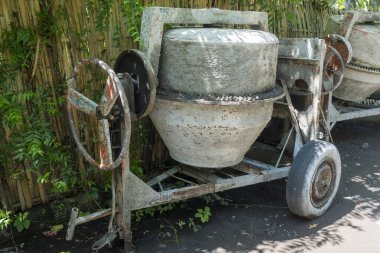 Paslı tekerleği olan çimento karıştırıcısı bahçede duruyor. Tekerlek kayıp ve makine bakımsız.