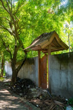 Tahta kapı bir duvarın önünde açık. Kapı ahşap ve çatısı var. Duvar betondan yapılmış ve yosunla kaplı.