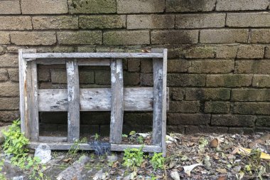 Ahşap sandık yerde tuğla bir duvarın yanında duruyor. Sandık toprakla kaplı ve üzerinde birkaç parça çöp var. Sahne ihmalkarlık ve terk edilmedir.