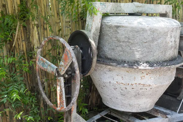 Paslı tekerleği olan çimento karıştırıcısı bahçede duruyor. Tekerlek kayıp ve makine bakımsız.