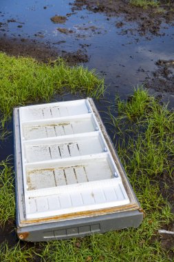 Dirty refrigerator door is sitting in a muddy field. The refrigerator is covered in mud and grass, and it is broken. The scene is desolate and abandoned