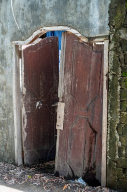 Tuğla duvarın önündeki kapı açık. Kapı eski ve paslı. Duvar yosunla kaplı.