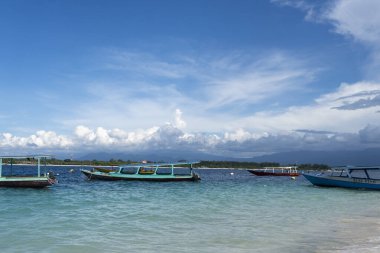 Gili, Lombok, Endonezya - 7 Ocak 2025: Mavi tekne beyaz bir şemsiyenin yanına yanaştı. Sahne huzurlu ve rahatlatıcı. Arka planda okyanus ve tekneler var.