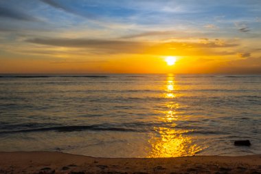 Güneş okyanusun üzerinde batıyor, suyun üzerine sıcak bir parıltı saçıyor. Gökyüzü mavi ve turuncunun karışımıdır. Huzurlu ve huzurlu bir atmosfer yaratır.
