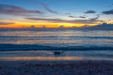Güneş okyanusun üzerinde batıyor, suyun üzerine sıcak bir parıltı saçıyor. Gökyüzü mavi ve turuncunun karışımıdır. Huzurlu ve huzurlu bir atmosfer yaratır.