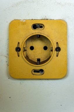 Ortasında bir delik olan sarı priz. Priz kirli ve ortasında bir delik var.