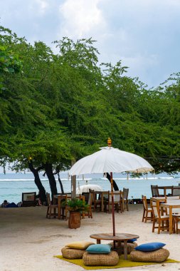 Beyaz şemsiyeli plaj sahnesi ve sandalyeli masalar. Sahne rahat ve davetkar.