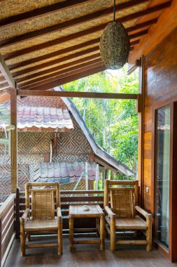 İki sandalyeli ahşap bir bank ve dışarıda bir masa var. Bankta bir veranda var ve sandalyeler sokağa bakıyor.