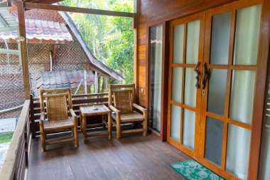 İki sandalyeli ahşap bir bank ve dışarıda bir masa var. Bankta bir veranda var ve sandalyeler sokağa bakıyor.